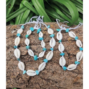 May include: Three white shell anklets with turquoise beads on a brown wooden surface.