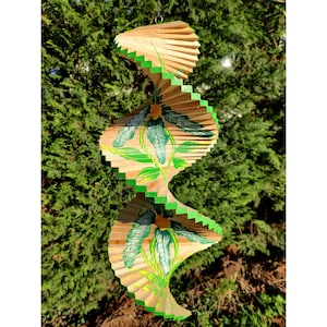 Könnte beinhalten: Ein Holz-Spiralwindspiel mit grünen und weißen Blumendesigns. Das Windspiel besteht aus mehreren Holzlatten, die zu einer Spiralform verbunden sind. Die Blumendesigns sind auf die Latten gemalt und von allen Seiten des Windspiels sichtbar.