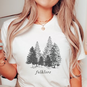 May include: White t-shirt with a black and white graphic of a forest with the word "folklore" printed below the graphic.