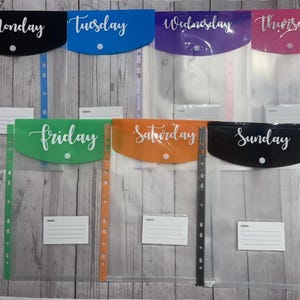 May include: Seven clear plastic folders with a pocket on the front. Each folder has a different colour and a day of the week printed on the front. The colours are black, blue, purple, pink, green, orange, and black. The days of the week are Monday, Tuesday, Wednesday, Thursday, Friday, Saturday, and Sunday.