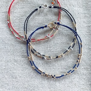 May include: Three bracelets with gold and silver beads and a red, black, and blue cord.