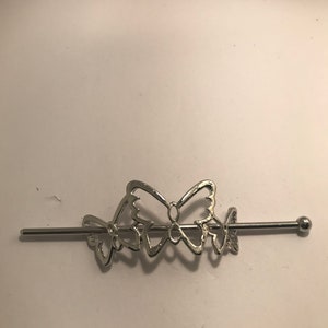 May include: Silver hair stick with three butterfly designs. The butterflies are connected to a thin metal rod with a small ball at the end.