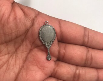 May include: A silver-toned hand mirror charm with an ornate design. The mirror is oval-shaped and has a small handle.