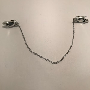 May include: A silver chain with two hand-shaped clasps. The chain is about 18 inches long.