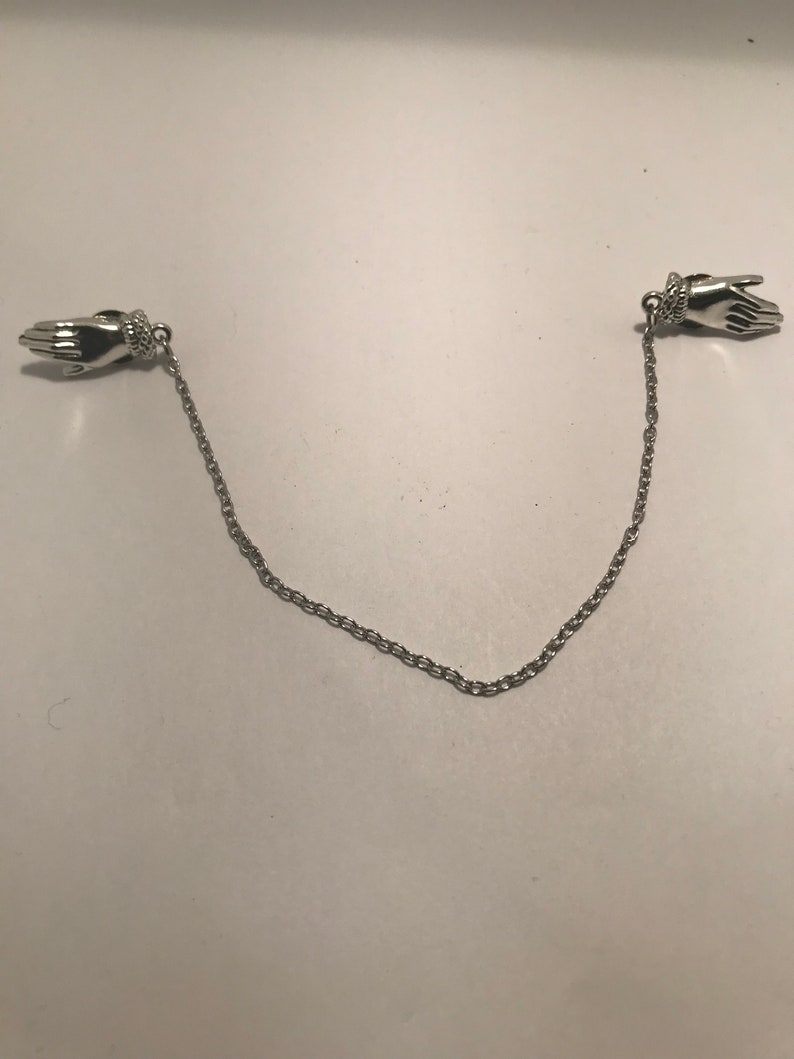May include: A silver chain with two hand-shaped clasps. The chain is about 18 inches long.