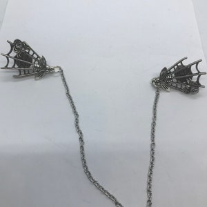 May include: A pair of silver-toned bee and spider web shaped brooches connected by a silver chain.