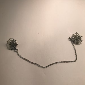 Puede incluir: Una cadena de plata con dos dijes en forma de telaraña. La cadena mide aproximadamente 30 cm de largo.