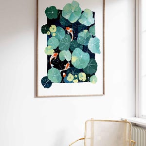 May include: A framed watercolor painting of a pond scene with koi fish and lily pads. The artwork features green lily pads, orange and white koi fish, and a dark blue background. The frame is a light brown color.