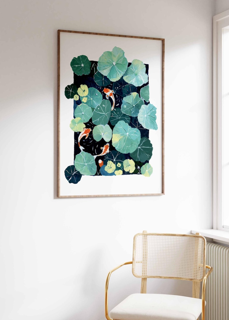 May include: A framed watercolor painting of a pond scene with koi fish and lily pads. The artwork features green lily pads, orange and white koi fish, and a dark blue background. The frame is a light brown color.