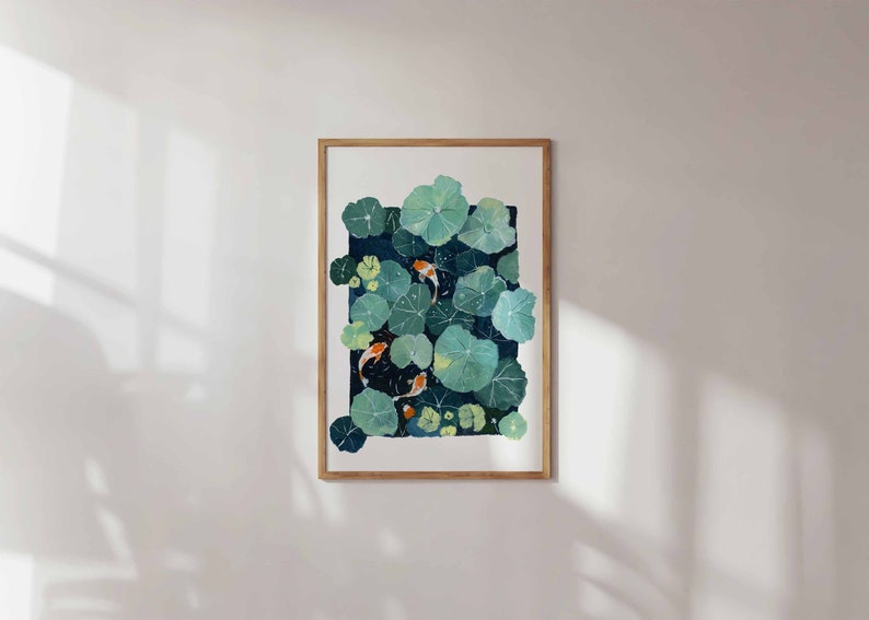 May include: A framed art print featuring a watercolor painting of lily pads and koi fish. The artwork showcases large, round, green lily pads with orange and white koi fish swimming beneath them. The frame is made of light brown wood.