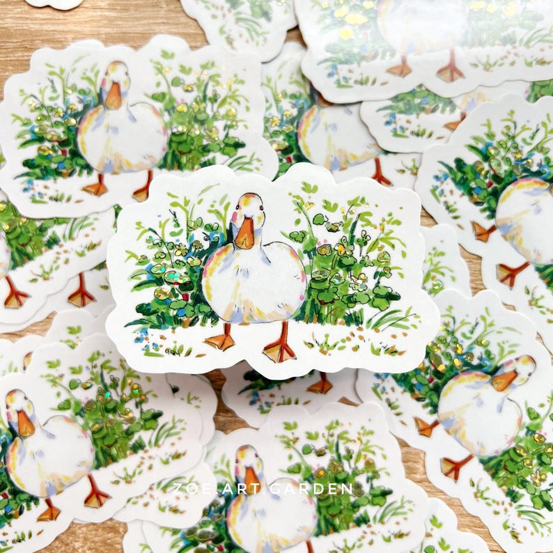 A white vinyl sticker with a white duck in green foliage is centered among many identical stickers on a light wooden surface, with a watermark at the bottom.