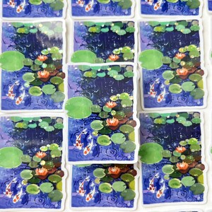 A close-up, overhead view of multiple rectangular stickers with white borders, each depicting two koi fish in a pond with lily pads and water lilies, arranged in rows.
