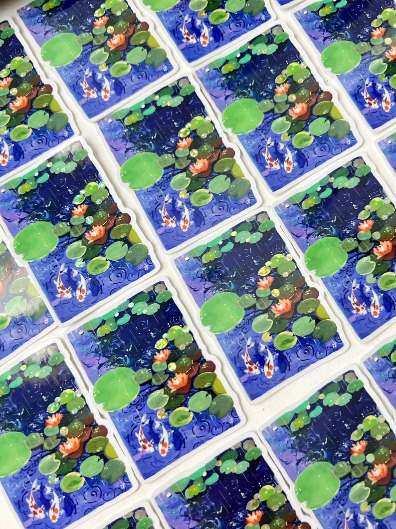 An overhead view of many rectangular stickers with white borders, each showing two koi fish in a pond with lily pads and water lilies, arranged in a grid pattern.