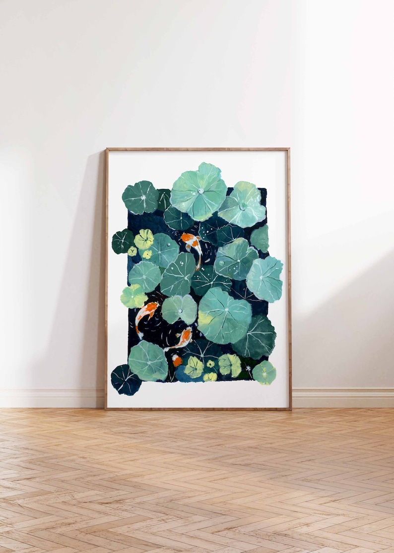 May include: A framed art print featuring a pond scene with koi fish and lily pads. The artwork depicts orange and white koi fish swimming among large, green lily pads. The background is a dark blue, creating a contrast with the bright fish and pads.