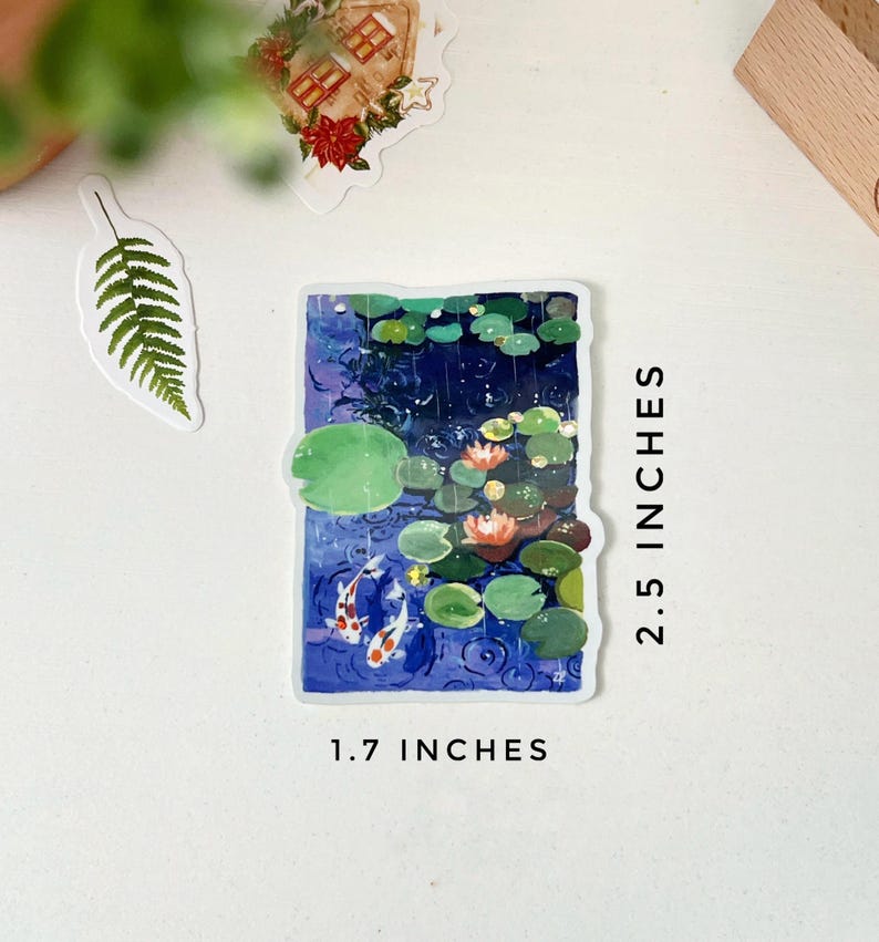 A rectangular sticker with a white border, showing two koi fish in a pond with lily pads and water lilies, is displayed next to text indicating its dimensions: "2.5 INCHES" and "1.7 INCHES."