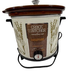 May include: A vintage Hamilton Beach Crock Watcher slow cooker with a 4-quart capacity. The off-white metal exterior features gold-toned botanical illustrations of thyme. It has a brown ceramic lid, black plastic handles, and a front control knob.