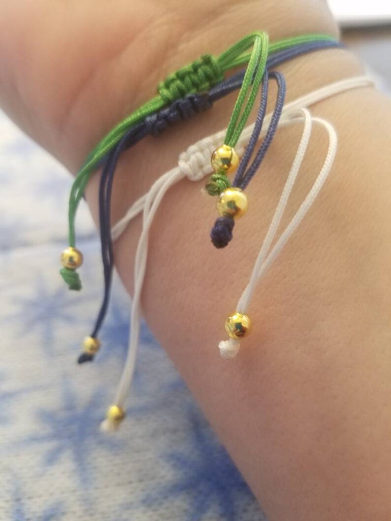 May include: A multi-colored friendship bracelet with green, blue, and white strings and gold beads.
