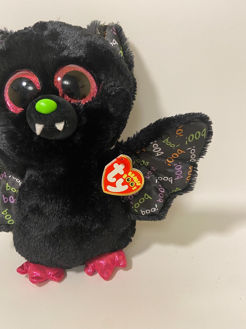 May include: Black plush bat with pink glitter eyes and a green nose. The bat has pink feet and a Ty Beanie Boo tag with the words "Boo!" and "004".