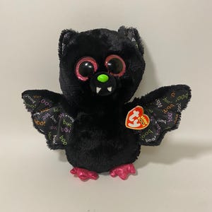 May include: Black plush bat with pink feet and wings. The bat has large, glittery eyes and a green nose. The wings are printed with the words "boo!" and "boo". The bat has a Ty tag attached to its right wing.