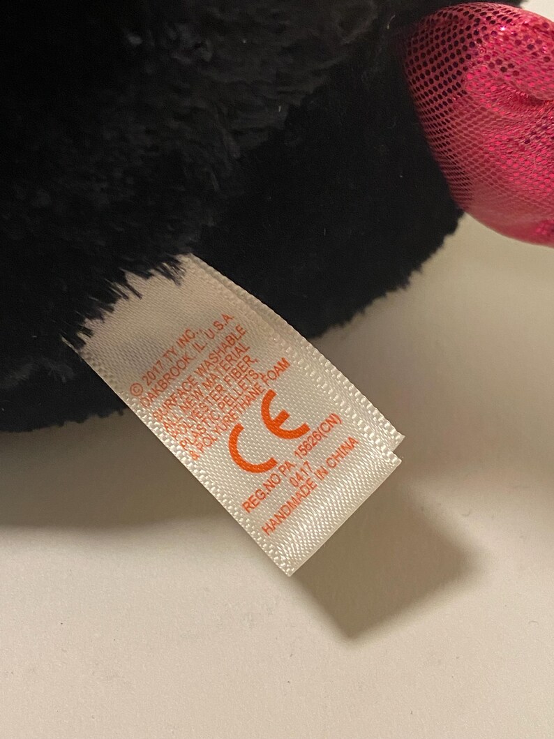 May include: A black and pink plush toy with a white tag that reads "2017 TY INC. SOAKBROOK, IL. U.S.A SURFACE WASHABLE CE REG.NO PA 15826(CN) 0417 HANDMADE IN CHINA"