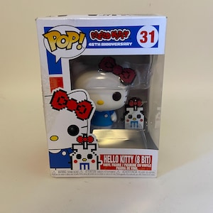 May include: A white Hello Kitty Pop! Vinyl figure with a red bow and blue dress. The figure is holding a smaller 8-bit Hello Kitty figure. The box is red, white, and blue with the text "Pop! Hello Kitty 45th Anniversary 31" on the front.