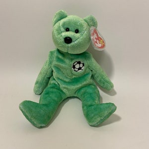 May include: Green Beanie Baby plush toy with a football on its chest. The toy has a red tag with a white star.