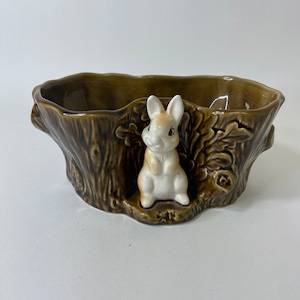 May include: A brown ceramic planter shaped like a tree stump with a white rabbit figurine peeking out from the side.