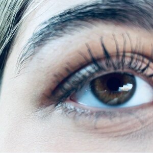 Peut inclure: Gros plan sur l'&oelig;il d'une personne avec de longs cils et un iris brun. L'&oelig;il regarde vers le haut et vers la droite.