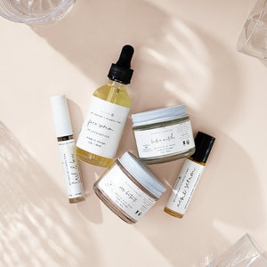 Peut inclure: Une collection de cinq produits de soin de la peau dans des flacons et des pots en verre avec des &eacute;tiquettes blanches. Les produits comprennent un s&eacute;rum pour le visage, un masque d'argile d&eacute;toxifiant, un masque d'argile doux, un s&eacute;rum pour les douleurs et un s&eacute;rum pour les cils et les sourcils. Les produits sont tous naturels et sans cruaut&eacute;.