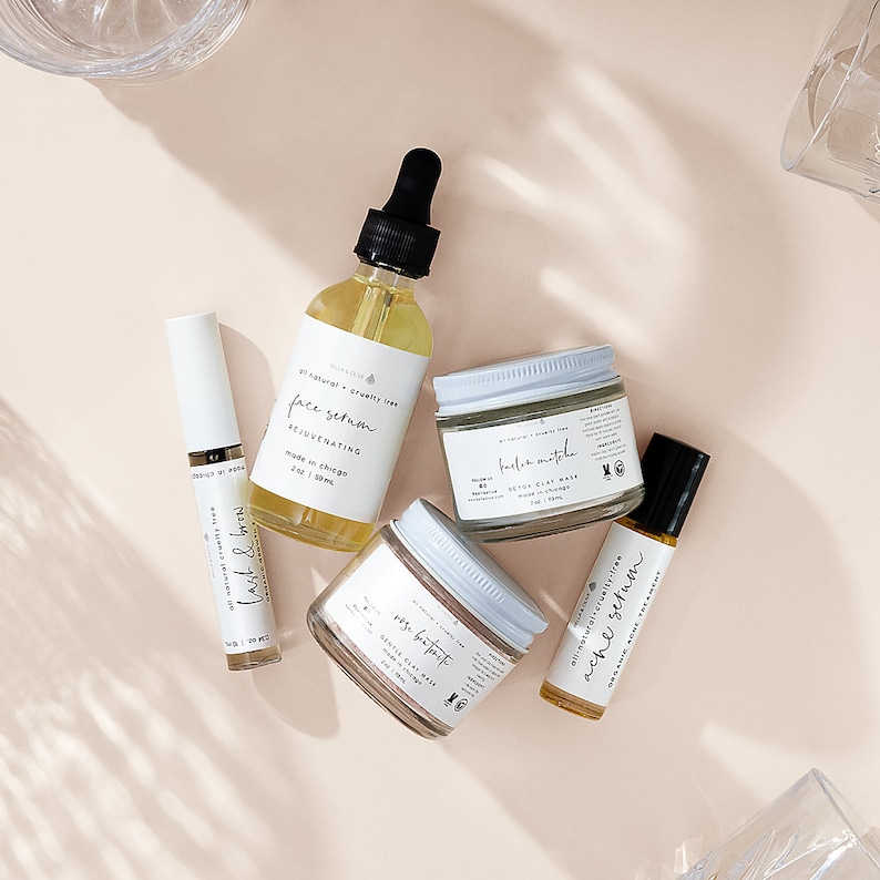 Peut inclure: Une collection de cinq produits de soin de la peau dans des flacons et des pots en verre avec des &eacute;tiquettes blanches. Les produits comprennent un s&eacute;rum pour le visage, un masque d'argile d&eacute;toxifiant, un masque d'argile doux, un s&eacute;rum pour les douleurs et un s&eacute;rum pour les cils et les sourcils. Les produits sont tous naturels et sans cruaut&eacute;.