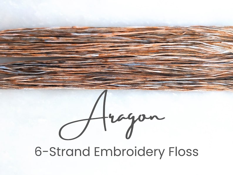 May include: A close-up of a skein of six-strand embroidery floss in a brown and white colorway. The floss is labeled "Aragon" and is described as "6-Strand Embroidery Floss".