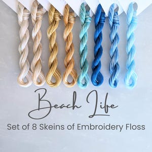 May include: A set of eight skeins of embroidery floss in a range of colors, from cream and gold to shades of blue. The text "Beach Life" and "Set of 8 Skeins of Embroidery Floss" are displayed below the floss.