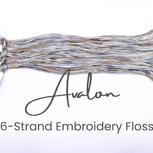 May include: Six strands of embroidery floss in a light blue, brown, and white color scheme. The floss is labeled "Avalon 6-Strand Embroidery Floss".