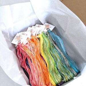 Puede incluir: Una caja llena de carretes de hilo de bordar de colores. El hilo est&aacute; dispuesto en forma de arco&iacute;ris, con cada carrete etiquetado con el nombre del color.