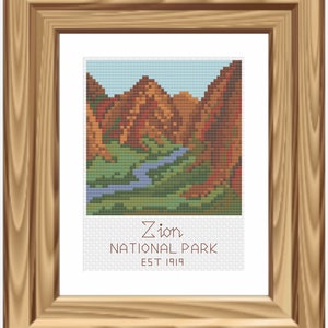 May include: A framed cross-stitch artwork depicting a scenic view of Zion National Park. The image shows a river winding through a canyon with red rock cliffs on either side. The text below the image reads "Zion National Park Est 1919".