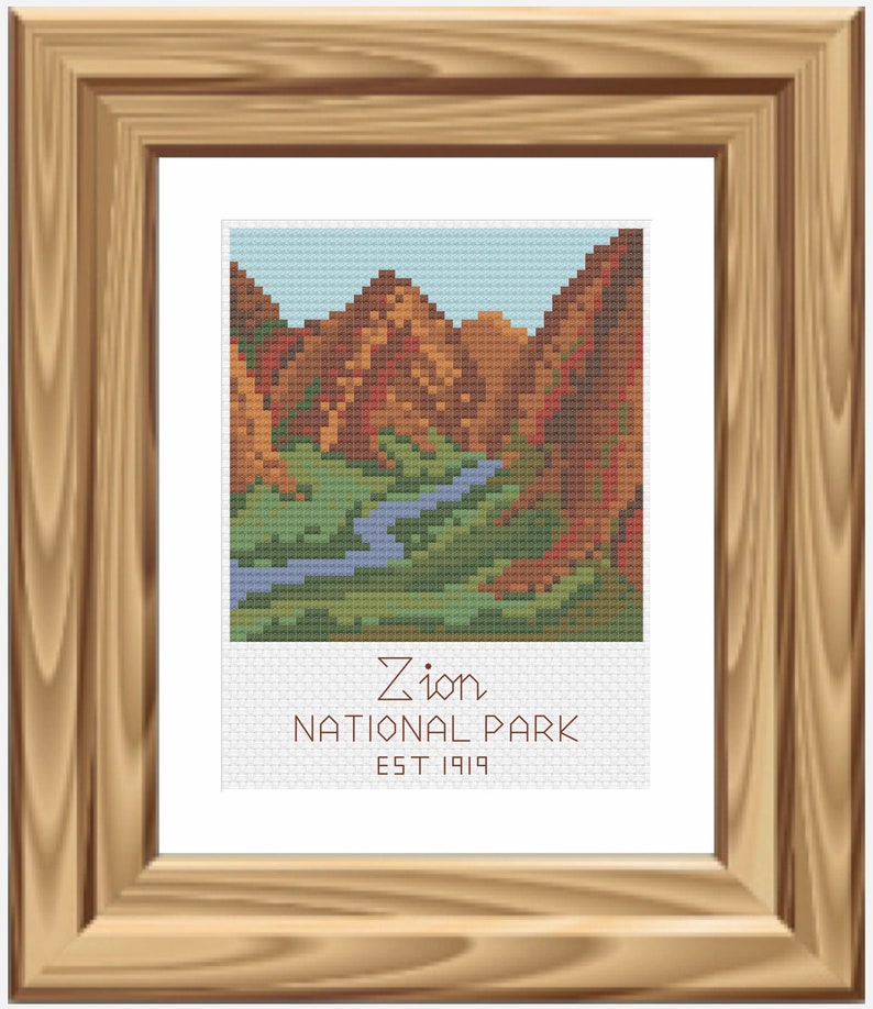 May include: A framed cross-stitch artwork depicting a scenic view of Zion National Park. The image shows a river winding through a canyon with red rock cliffs on either side. The text below the image reads "Zion National Park Est 1919".
