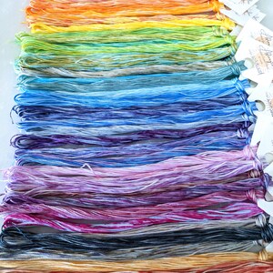 Puede incluir: Una colecci&oacute;n de madejas de hilo de bordar de colores, dispuestas en un patr&oacute;n de arco&iacute;ris. El hilo est&aacute; te&ntilde;ido a mano y tiene un aspecto jaspeado.