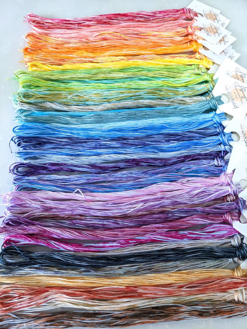 Puede incluir: Una colecci&oacute;n de madejas de hilo de bordar de colores, dispuestas en un patr&oacute;n de arco&iacute;ris. El hilo est&aacute; te&ntilde;ido a mano y tiene un aspecto jaspeado.