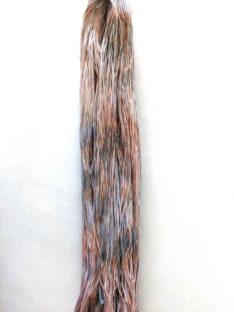 May include: A skein of yarn in shades of brown, blue, and white. The yarn is hand-dyed and has a variegated color pattern.