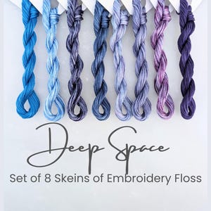 May include: A set of eight skeins of embroidery floss in shades of blue, purple, and lavender. The floss is arranged vertically, with each skein displaying a different color variation. The text "Deep Space" and "Set of 8 Skeins of Embroidery Floss" are displayed.