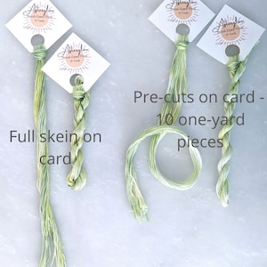 May include: Three skeins of green hand-dyed embroidery floss. One skein is full, and two are pre-cut into 10 one-yard pieces. The floss is labeled "Afterglow Hand-Dyed Floss 10 Yards".