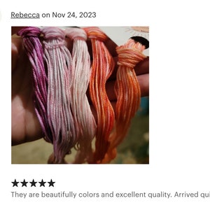 May include: Four skeins of embroidery floss in shades of pink, orange, and red. The floss is arranged in a hand, with the ends of the skeins tied together.