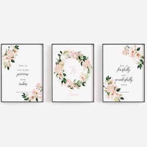 Puede incluir: Tres impresiones enmarcadas con diseños florales y citas inspiradoras. La primera impresión presenta una corona floral con la letra "A" en el centro y el texto "Anna". La segunda impresión presenta un diseño floral con la cita "Ella es mucho más preciosa que los rubíes." La tercera impresión presenta un diseño floral con la cita "Ella es hecha de manera temible y maravillosa."