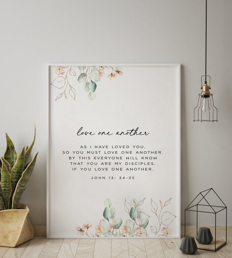 May include: A white framed print with a watercolour floral design and the text "love one another." The text continues with a bible verse from John 13:34-35: "As I have loved you, so you must love one another. By this everyone will know that you are my disciples, if you love one another."