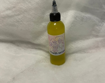 May include: A clear glass bottle with a black cap and a yellow liquid inside. The bottle has a label that says "growth serum" and features a floral design.