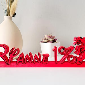 May include: Red wooden sign with the text "Ryanne 1%" and a red cartoon figure. The sign is on a white surface.