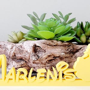 May include: Yellow wooden name sign with the name "Marlenis" in a whimsical font. The sign features a silhouette of a princess in a ball gown on the right side.