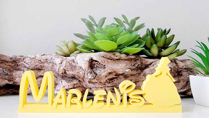 May include: Yellow wooden name sign with the name "Marlenis" in a whimsical font. The sign features a silhouette of a princess in a ball gown on the right side.