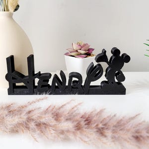 May include: Black wooden name sign with the name "Henry" spelled out in a stylised font. Mickey Mouse is featured on the right side of the sign.