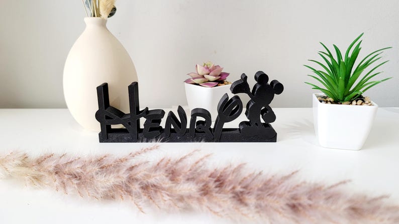 May include: Black wooden name sign with the name "Henry" spelled out in a stylised font. Mickey Mouse is featured on the right side of the sign.